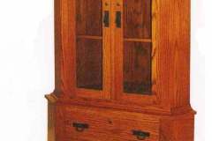 This Mission corner gun cabinet is shown crafted out of solid red oak.  The cabinet features two locking flush mounts doors with upper mullions and two full extension drawers with dovetailed construction in the lower cabinet.